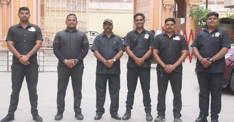 Six guards in dark uniforms standing in front of an ornate building