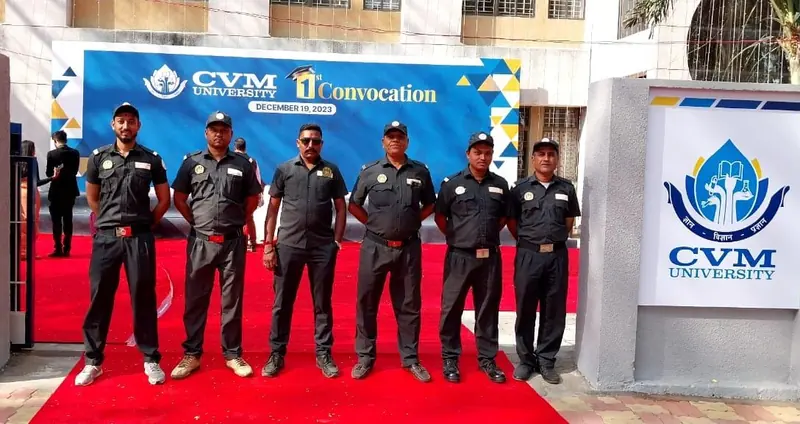 Guards in black uniforms standing on a red carpet beside a CVM University sign